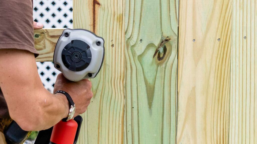 Man drilling screws into wood fence